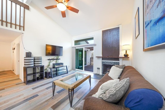 living room featuring high vaulted ceiling, light wood-type flooring, ceiling fan, and a fireplace