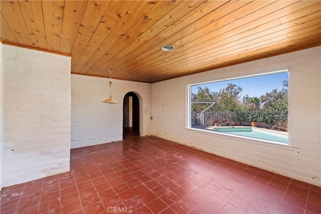 spare room featuring wooden ceiling and brick wall