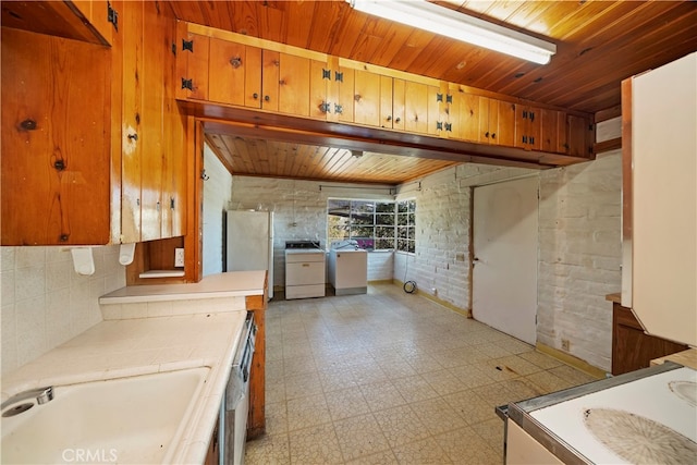 kitchen featuring sink, brick wall, stainless steel refrigerator, and washer / clothes dryer