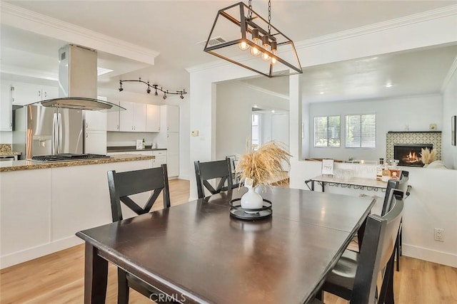 dining area featuring light hardwood / wood-style flooring, ornamental molding, a notable chandelier, and a fireplace