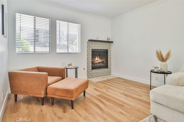 living area with wood-type flooring, crown molding, and a tiled fireplace