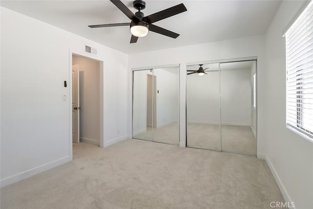 unfurnished bedroom featuring ceiling fan, light carpet, multiple windows, and two closets