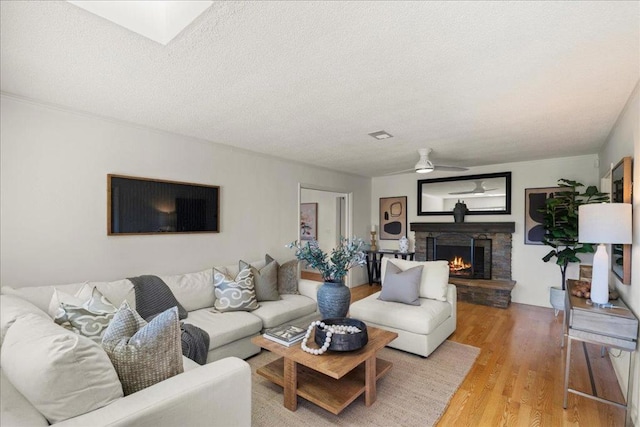 living room with ceiling fan, hardwood / wood-style floors, a textured ceiling, and a fireplace