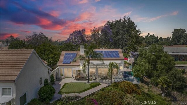 back house at dusk featuring a patio area and solar panels