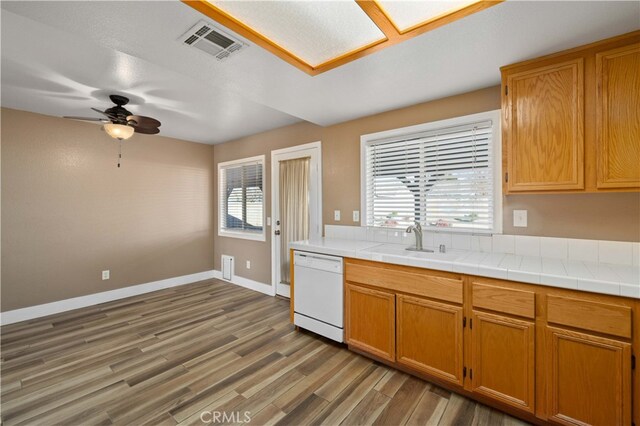 kitchen featuring ceiling fan, wood-type flooring, sink, white dishwasher, and tile counters