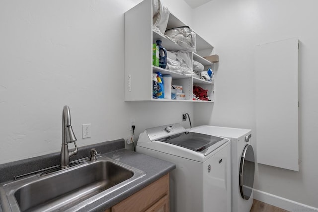 clothes washing area with washing machine and dryer, cabinets, wood-type flooring, and sink