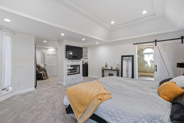 carpeted bedroom featuring connected bathroom, a fireplace, a barn door, and a tray ceiling