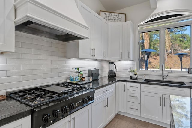 kitchen with premium range hood, white cabinetry, gas cooktop, and sink