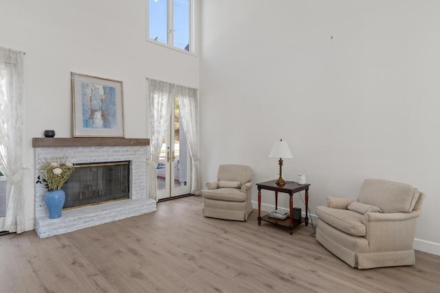 sitting room featuring a brick fireplace, light hardwood / wood-style flooring, and a towering ceiling