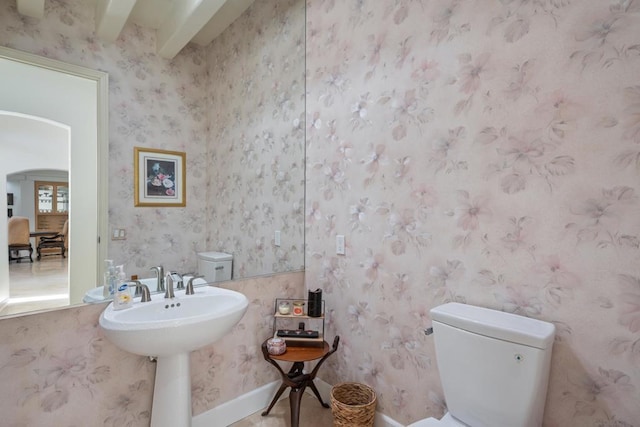 bathroom with sink, toilet, and beamed ceiling