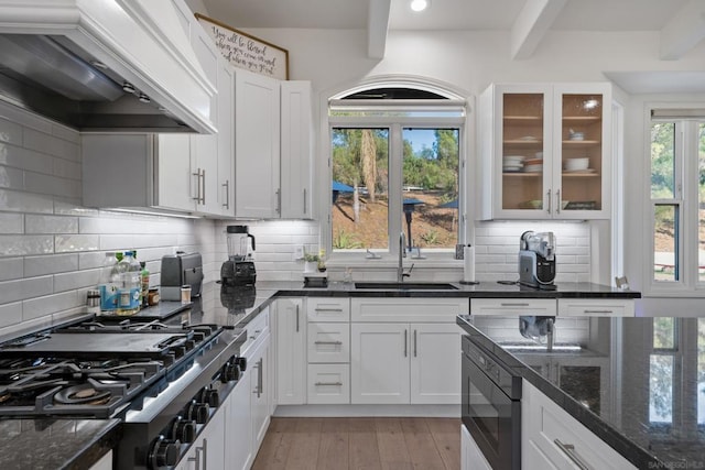 kitchen featuring custom exhaust hood, gas cooktop, dark stone countertops, white cabinets, and sink