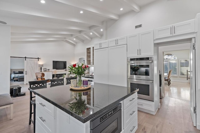 kitchen with a barn door, beamed ceiling, built in microwave, white cabinets, and double oven