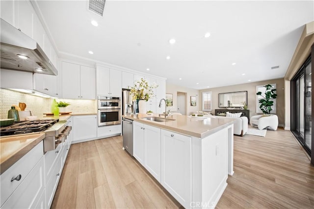 kitchen with white cabinetry, light hardwood / wood-style floors, ventilation hood, a kitchen island with sink, and sink