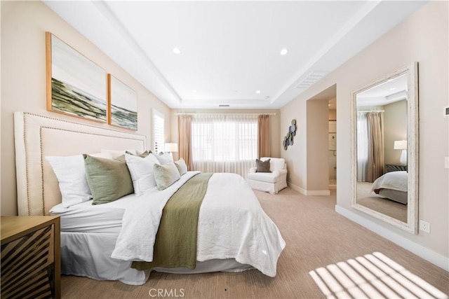 bedroom featuring ensuite bath, light carpet, and a raised ceiling