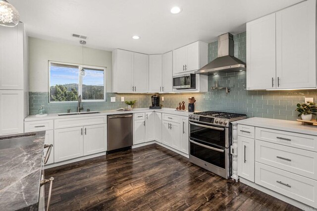 kitchen featuring appliances with stainless steel finishes, pendant lighting, white cabinetry, sink, and wall chimney range hood