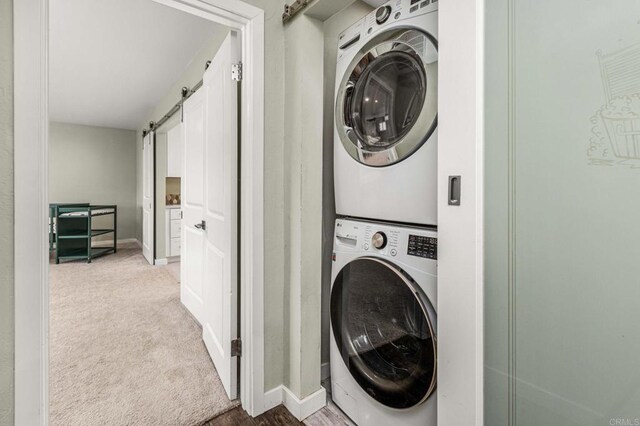 clothes washing area featuring a barn door, stacked washer / drying machine, and light carpet