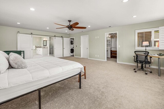 bedroom featuring stacked washer and dryer, ensuite bath, a spacious closet, light carpet, and a barn door