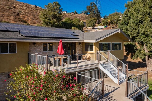 rear view of property with a wooden deck and solar panels