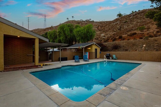 pool at dusk featuring an outdoor structure and a patio area