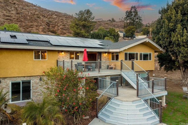2846 Willow Glen Dr, El Cajon, CA 92019 - back of property at dusk featuring stairway, stone siding, solar panels, and stucco siding