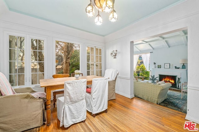 dining space featuring beam ceiling, a healthy amount of sunlight, an inviting chandelier, and hardwood / wood-style flooring