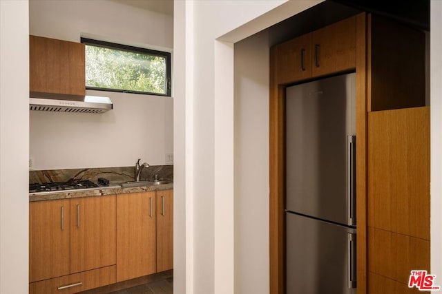 kitchen with exhaust hood, stainless steel appliances, dark stone counters, and sink