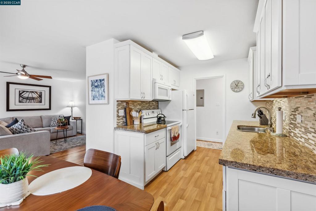 kitchen featuring sink, white cabinets, dark stone counters, and white appliances