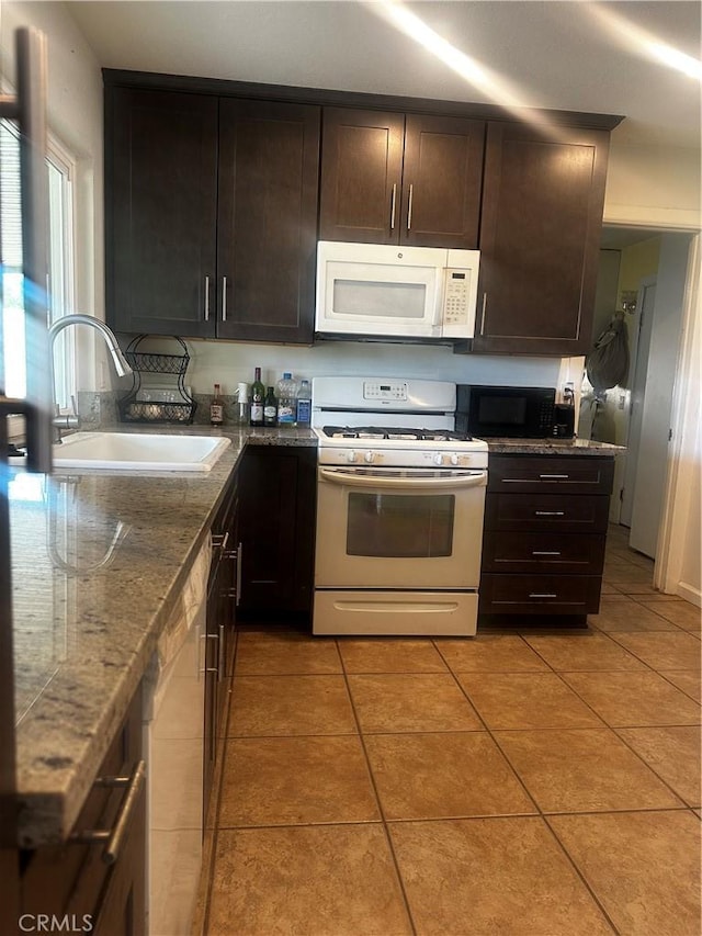 kitchen featuring dark brown cabinetry, sink, light tile patterned floors, white appliances, and dark stone counters