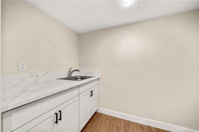 laundry area featuring a sink, baseboards, and light wood-style flooring