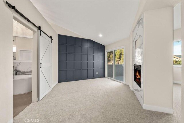 unfurnished living room featuring lofted ceiling, carpet flooring, a barn door, and a large fireplace