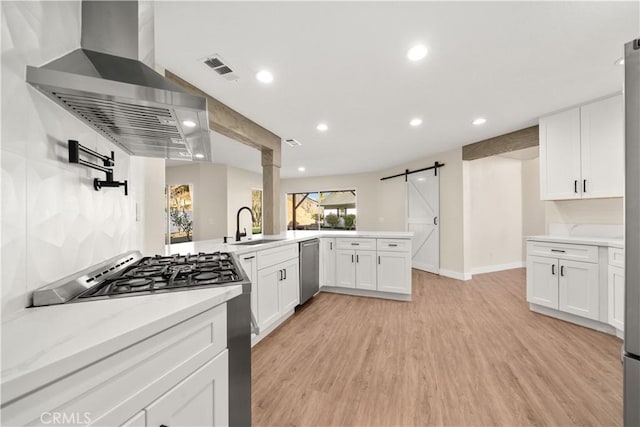 kitchen with a barn door, exhaust hood, appliances with stainless steel finishes, white cabinets, and light stone counters