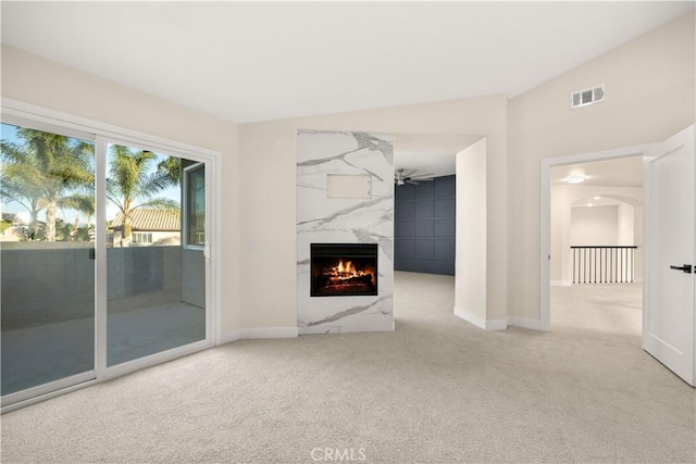 unfurnished living room with ceiling fan, vaulted ceiling, a high end fireplace, and light carpet