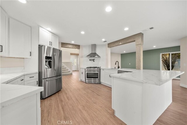 kitchen with appliances with stainless steel finishes, wall chimney range hood, a sink, white cabinets, and recessed lighting