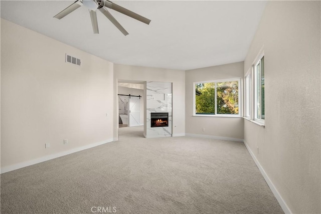 unfurnished living room with ceiling fan, light colored carpet, a high end fireplace, and a barn door