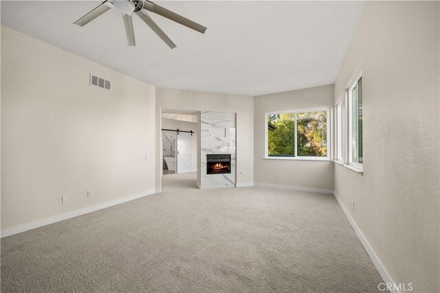 unfurnished living room featuring light colored carpet, a ceiling fan, baseboards, and a high end fireplace