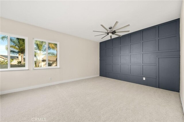 carpeted empty room with a decorative wall, a ceiling fan, and baseboards