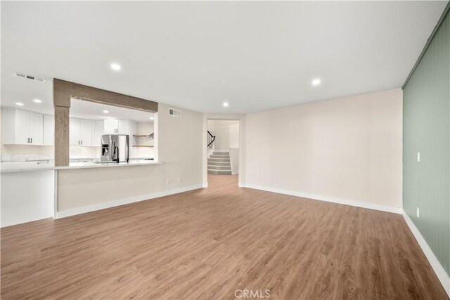 unfurnished living room with light wood-type flooring, stairs, recessed lighting, and baseboards