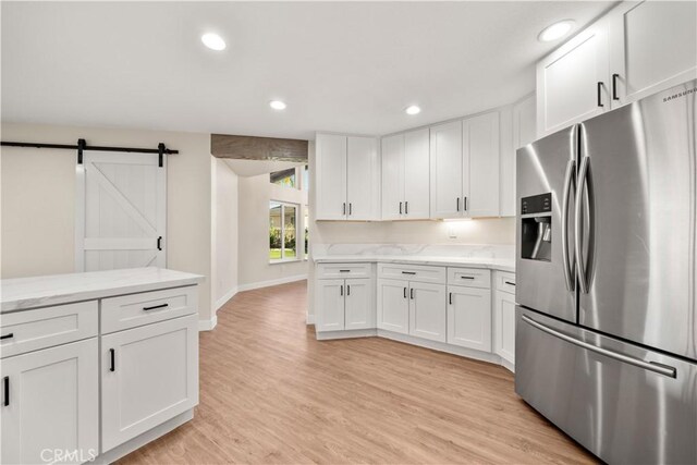kitchen featuring stainless steel refrigerator with ice dispenser, a barn door, white cabinets, light wood-style floors, and recessed lighting