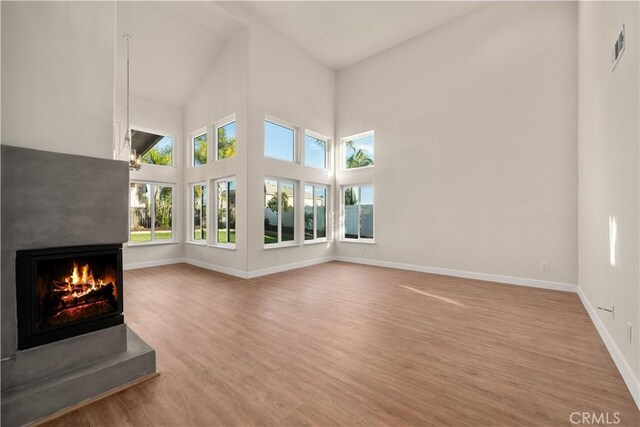 unfurnished living room featuring a multi sided fireplace, wood finished floors, baseboards, and high vaulted ceiling