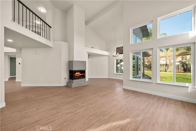 unfurnished living room featuring a multi sided fireplace, light hardwood / wood-style floors, and a towering ceiling