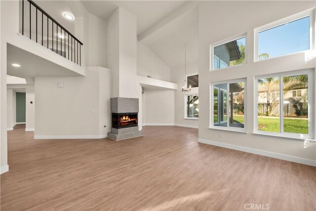 unfurnished living room featuring high vaulted ceiling, wood finished floors, baseboards, and a multi sided fireplace