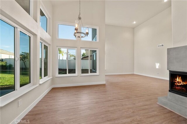 unfurnished living room with a chandelier, wood finished floors, a high ceiling, recessed lighting, and a multi sided fireplace