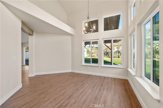unfurnished dining area with wood finished floors, a chandelier, a high ceiling, and baseboards