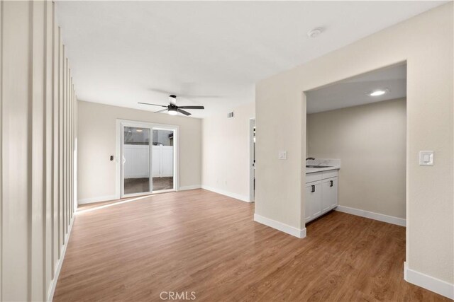 unfurnished room featuring a ceiling fan, light wood-style flooring, baseboards, and a sink
