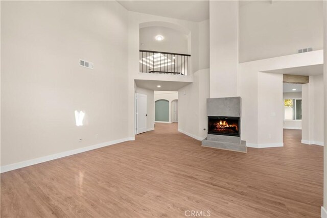 unfurnished living room with light wood finished floors, baseboards, a multi sided fireplace, a high ceiling, and arched walkways