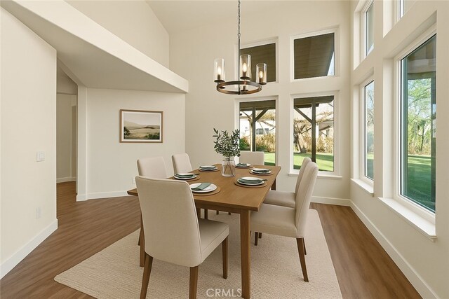 dining room with a chandelier, plenty of natural light, wood finished floors, and a high ceiling