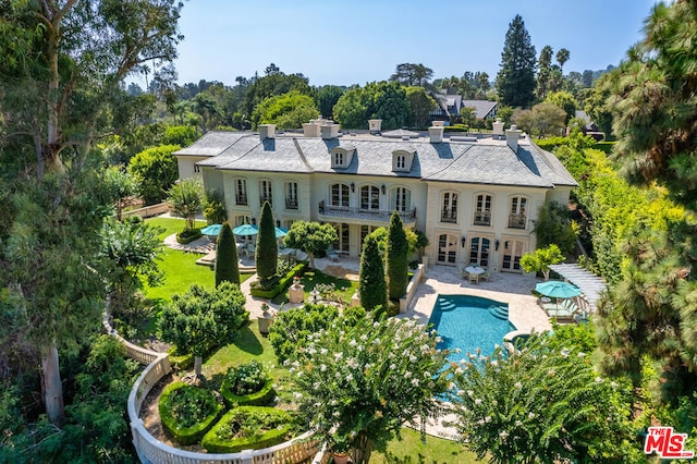 back of property with a balcony, a patio area, and a lawn