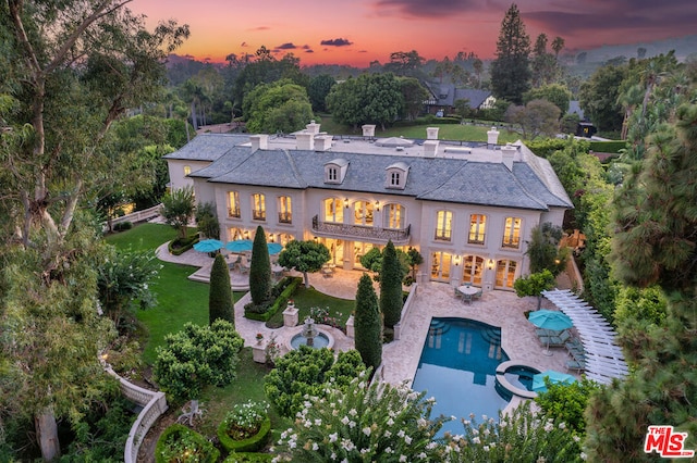 back house at dusk featuring a yard, a patio area, and a pool with hot tub