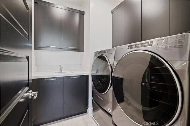 clothes washing area with cabinets, washing machine and clothes dryer, and sink