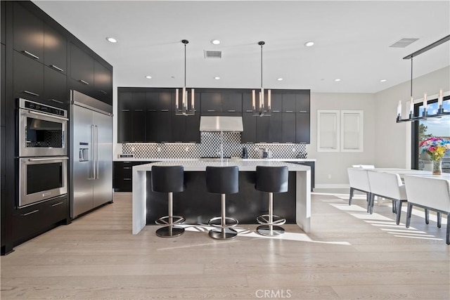 kitchen featuring a kitchen bar, hanging light fixtures, ventilation hood, and stainless steel appliances